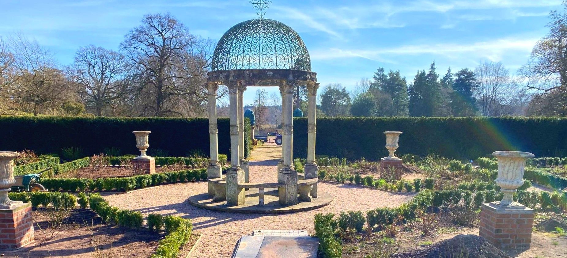 There is a gazebo in the middle of a garden surrounded by bushes.