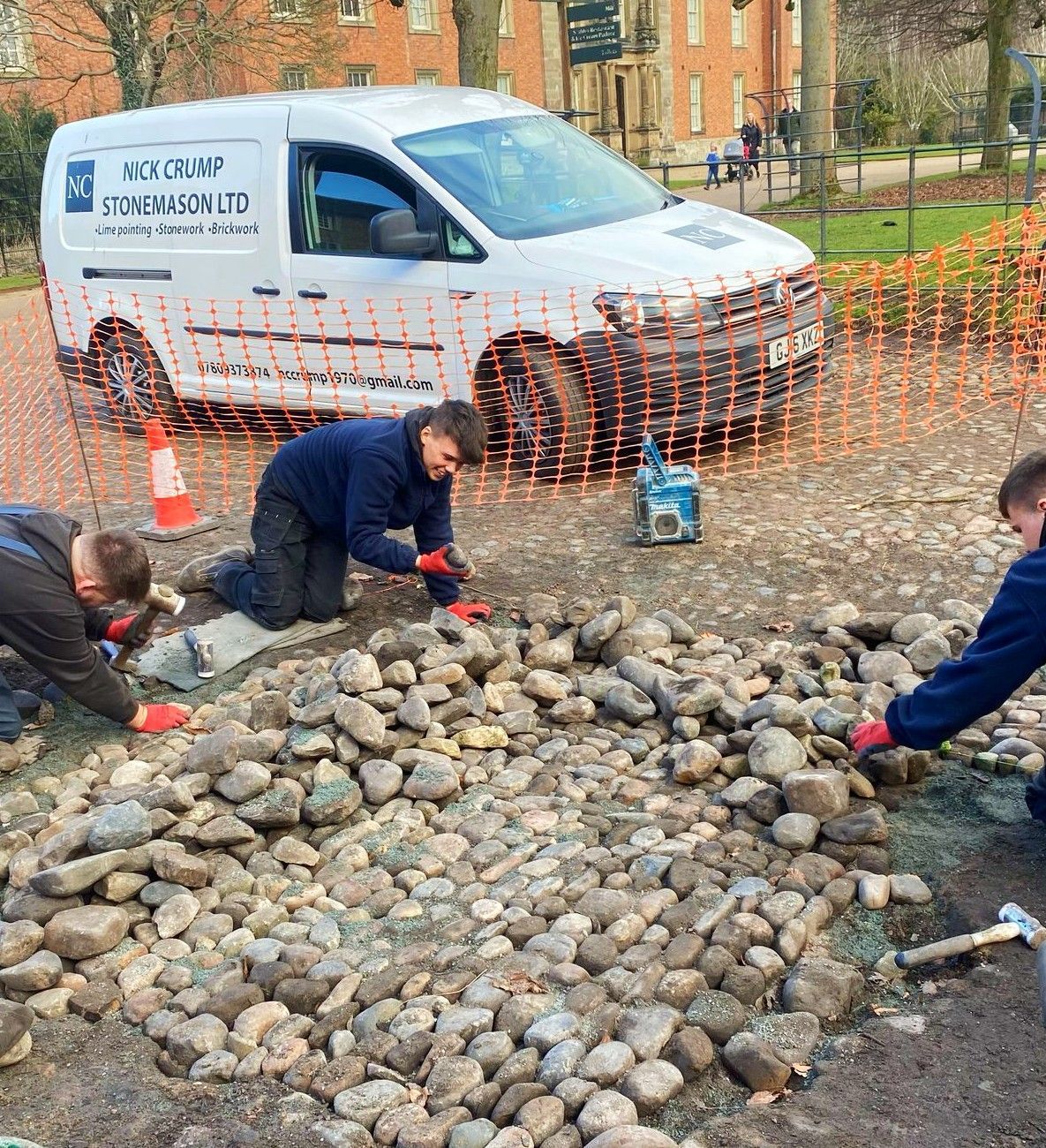 A group of people are working on a cobblestones rocky area in front of a van.