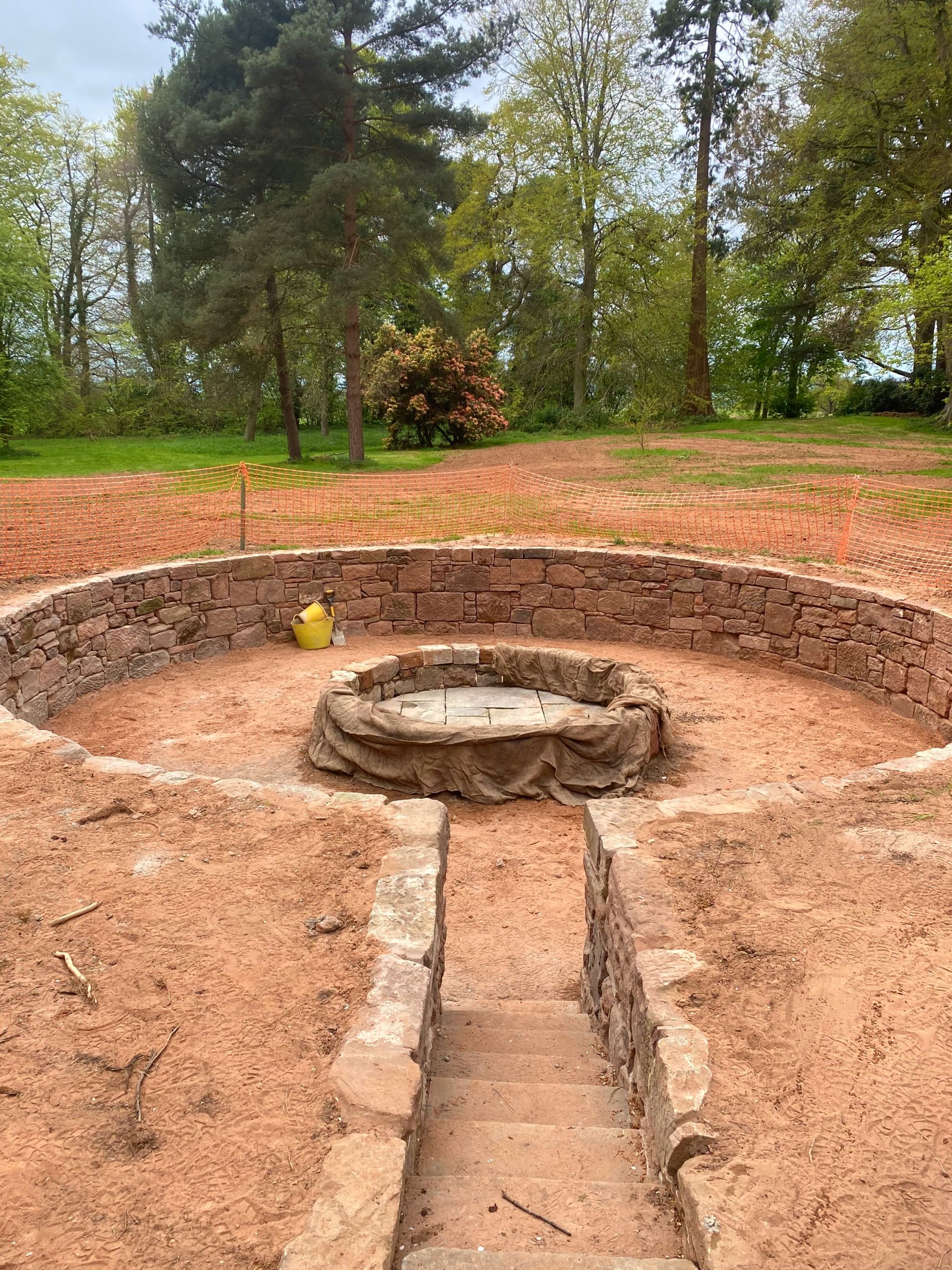 A stonewalled pit in the middle of a dirt field with trees in the background. . Stonemasons Cheshire