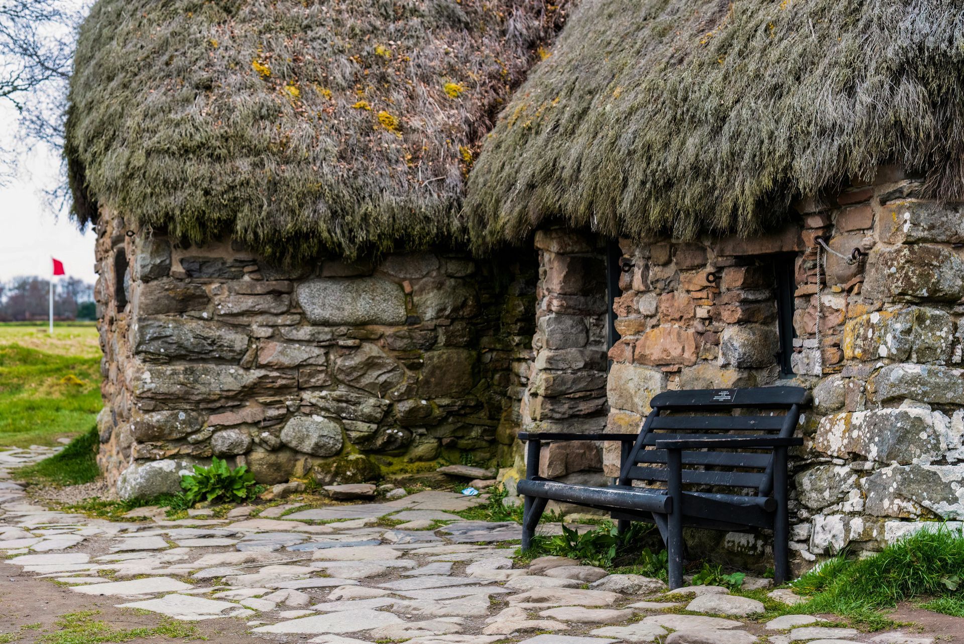 A stone building with a thatched roof and a bench in front of it.