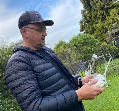Man in black jacket operates a drone controller in a grassy outdoor setting.