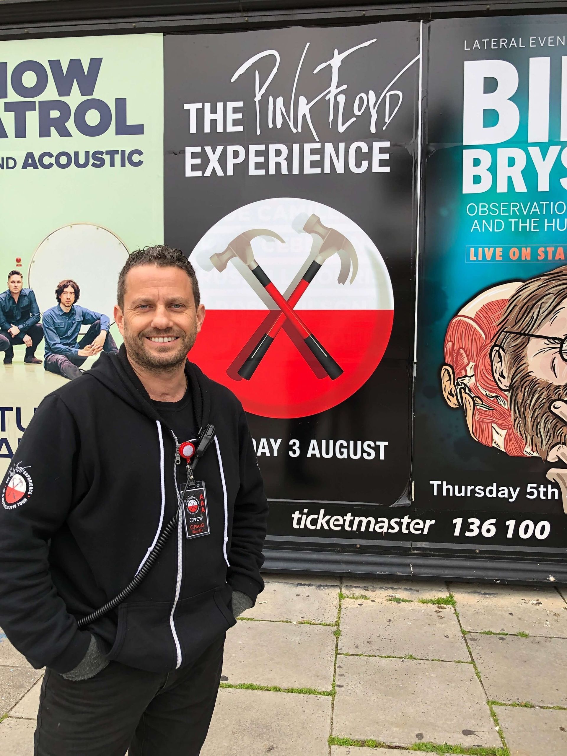 Craig Walsh smiles in front of Pink Floyd Experience, Snow Patrol, and Bill Bryson posters.