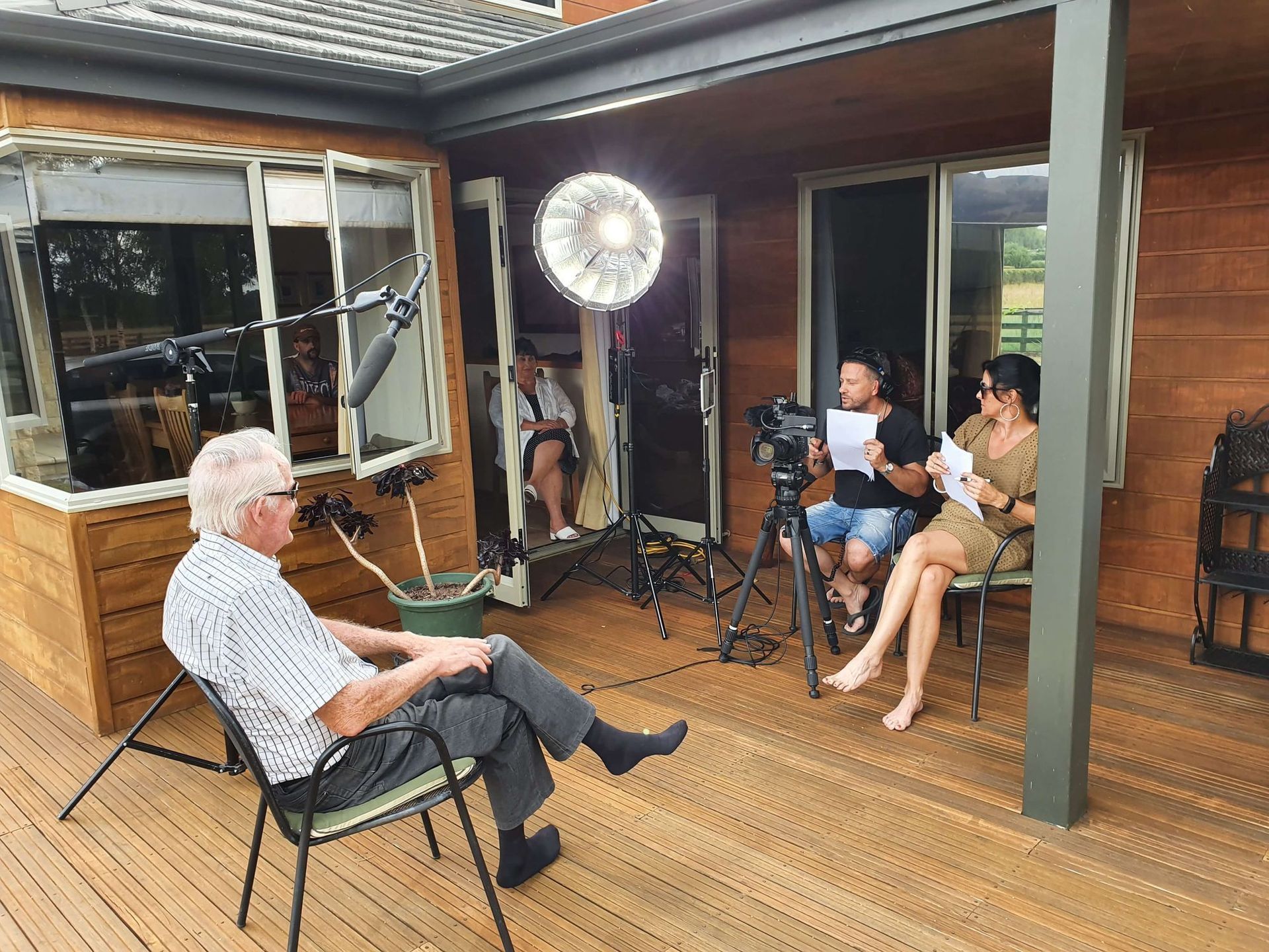People filming an interview outdoors: man speaking, other people with equipment, papers.