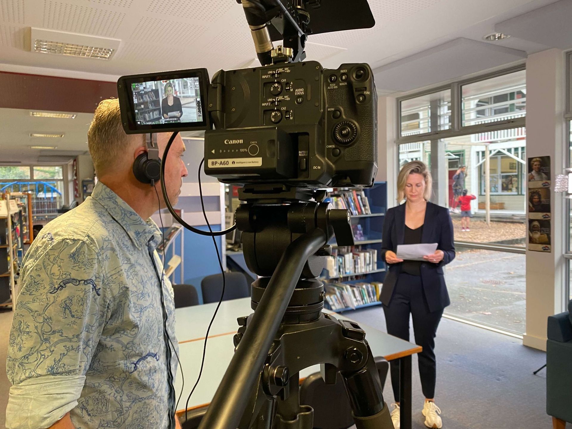 A person filming a woman in a library. The woman holds papers, speaking.