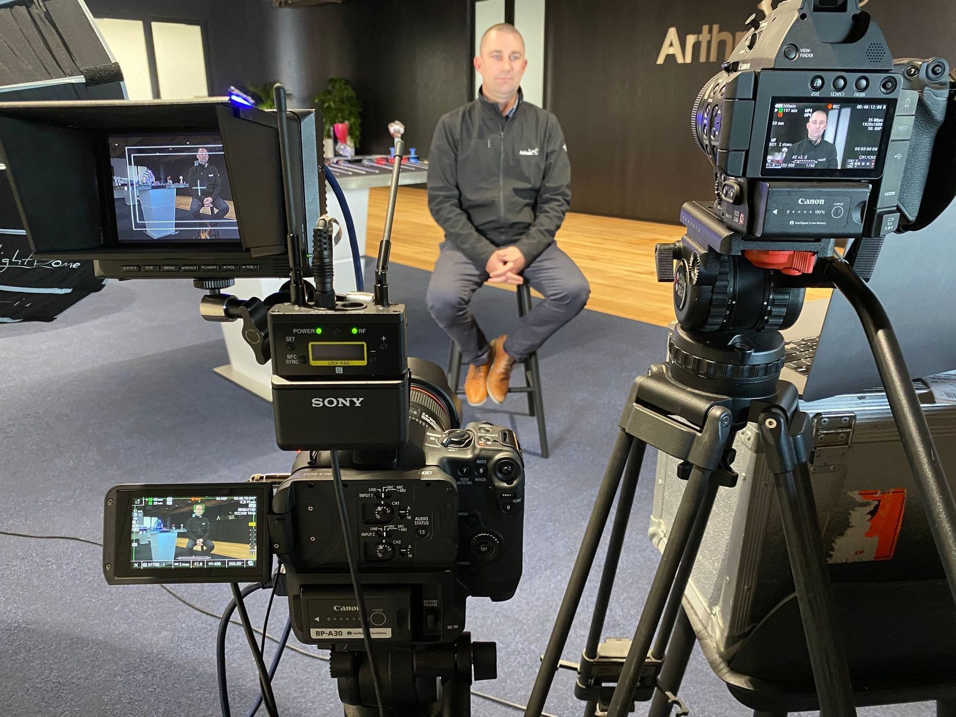 Man seated for an interview, surrounded by video cameras and equipment in a studio setting.