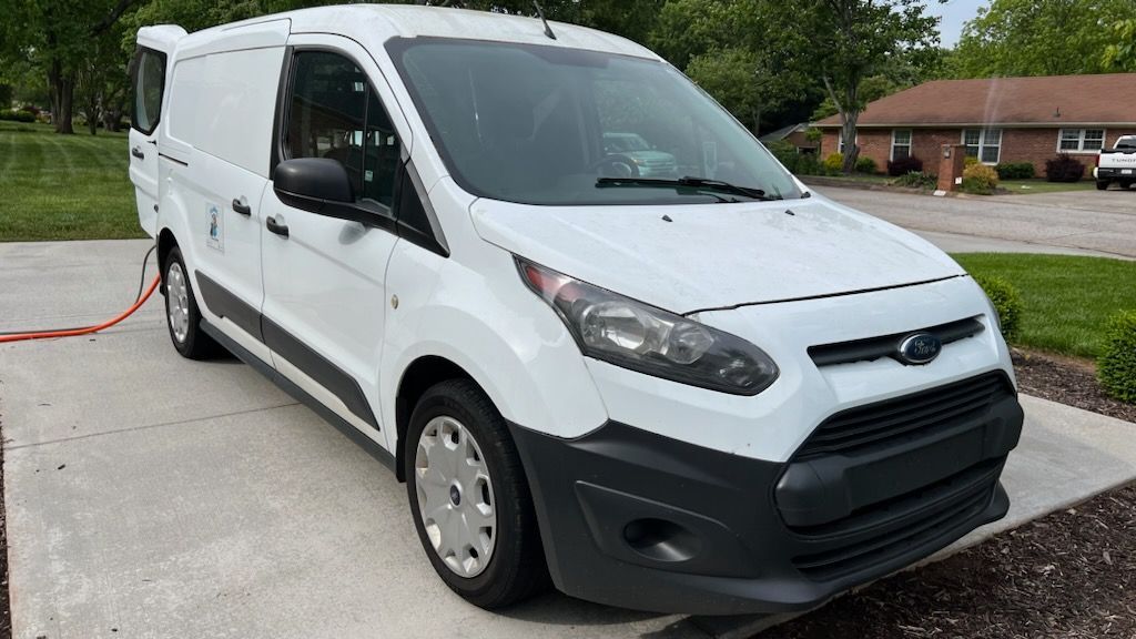 White cargo van parked outdoors on a wet lot, shown from the front-left side.