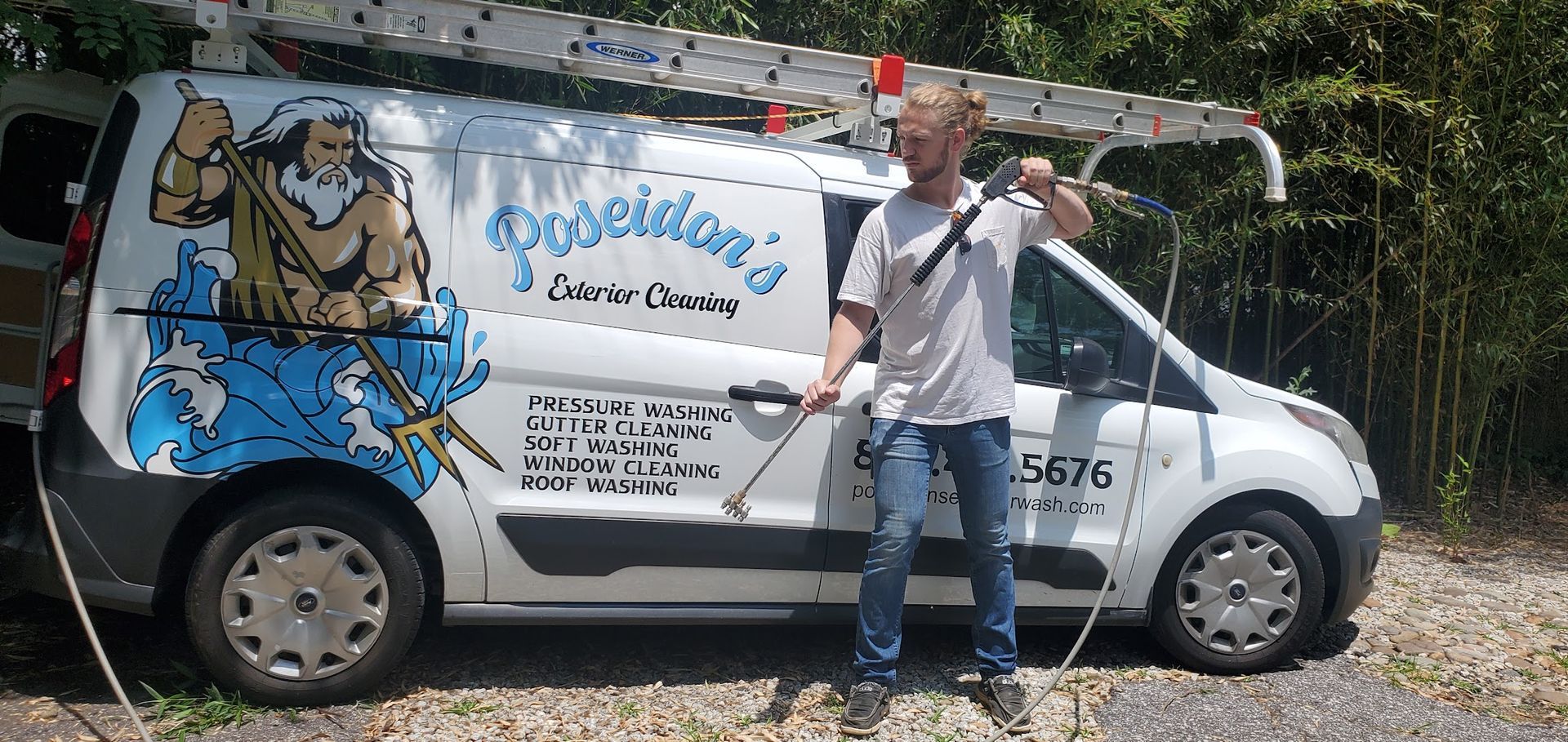 Man standing beside a white van with a large blue-and-brown mural on its side, outdoors on a gravel road.