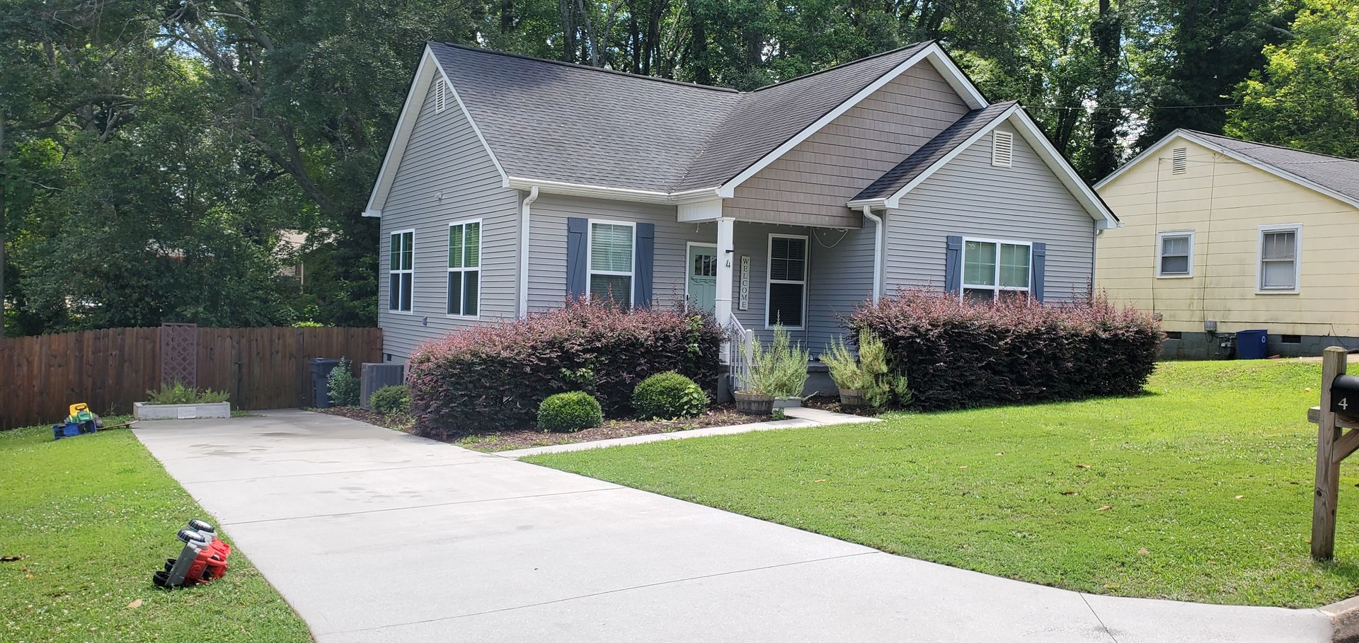 Suburban house with a long driveway, green lawn, and bushes under a partly cloudy sky