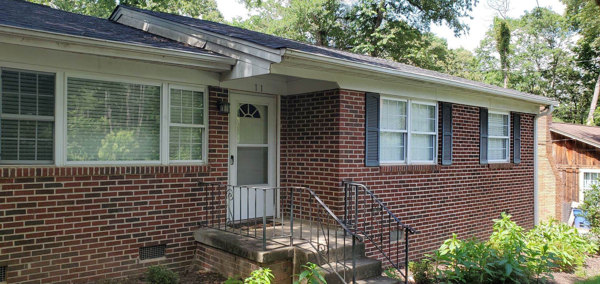 Brick house exterior with white-trim windows, front door, and steps under trees