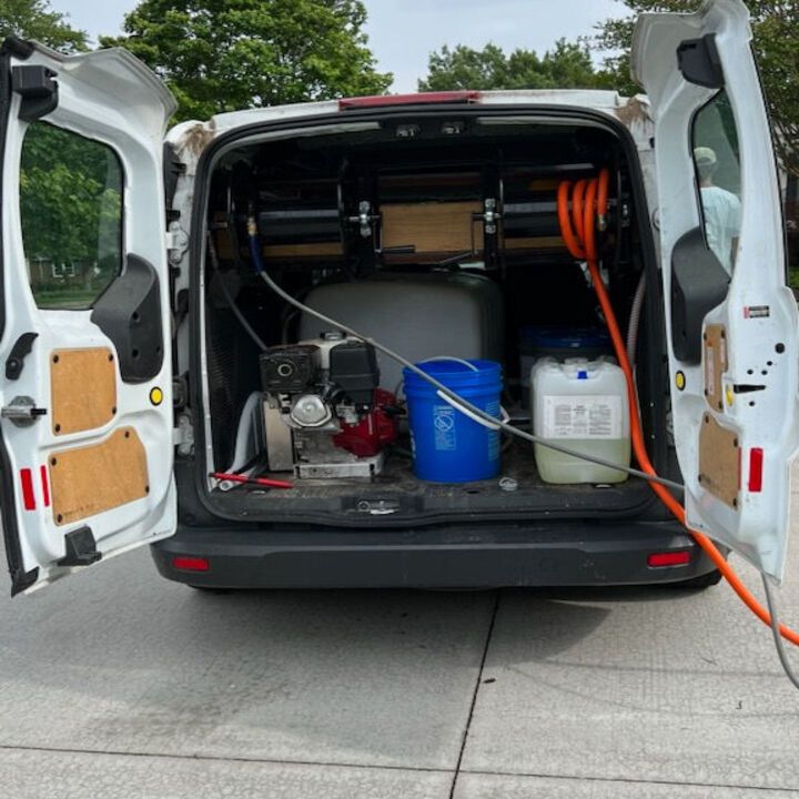 Open cargo van with cleaning equipment, blue bucket, tanks, and coiled orange hose inside.