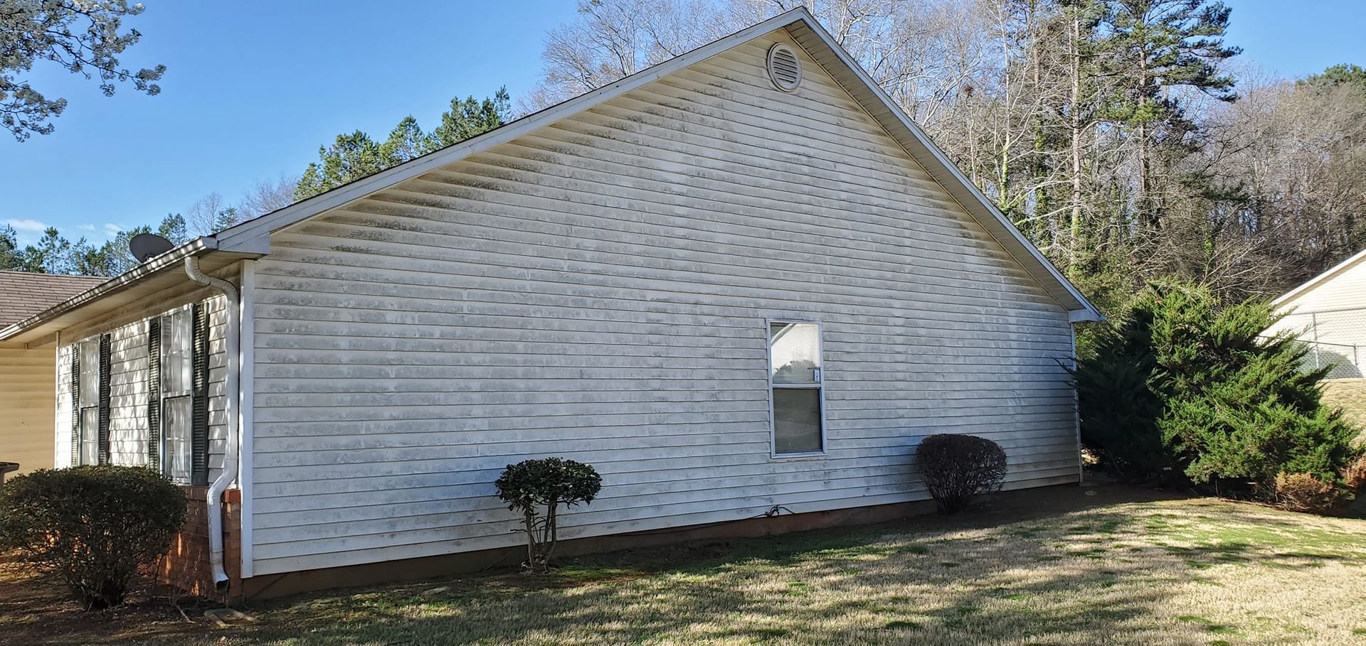 Side view of a white-sided house with small windows and trimmed shrubs in a sunny yard