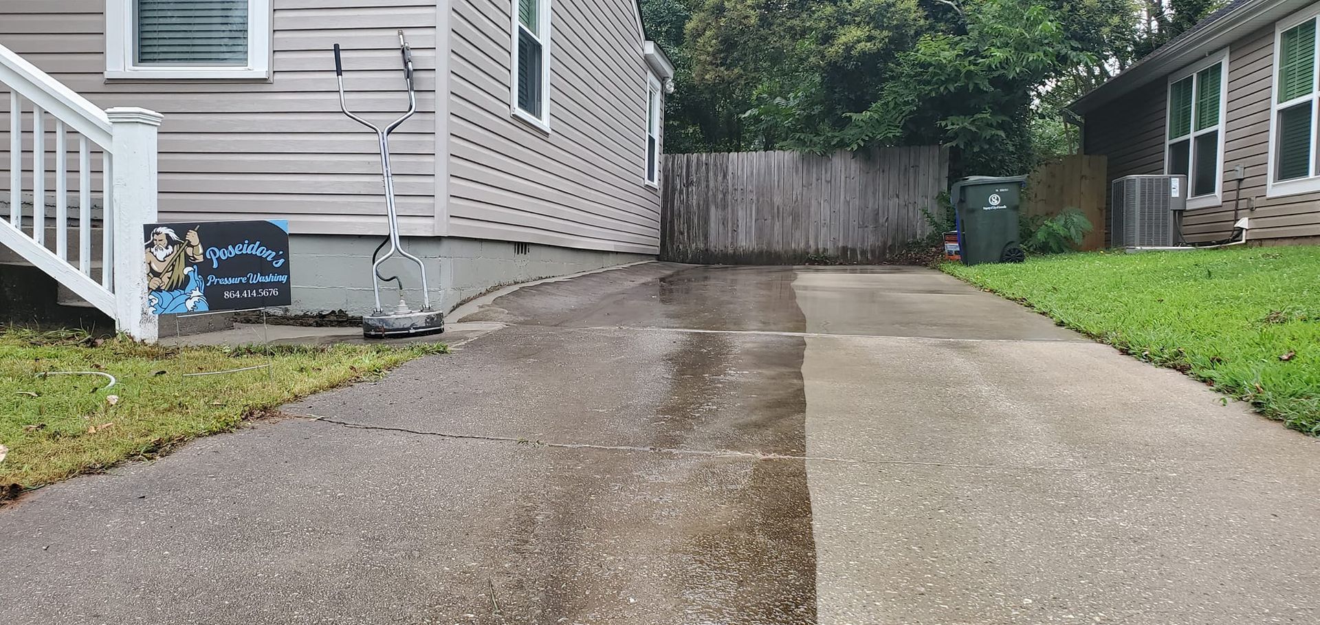 Driveway split between gravel and concrete beside a house, with wet pavement and a fenced backyard.