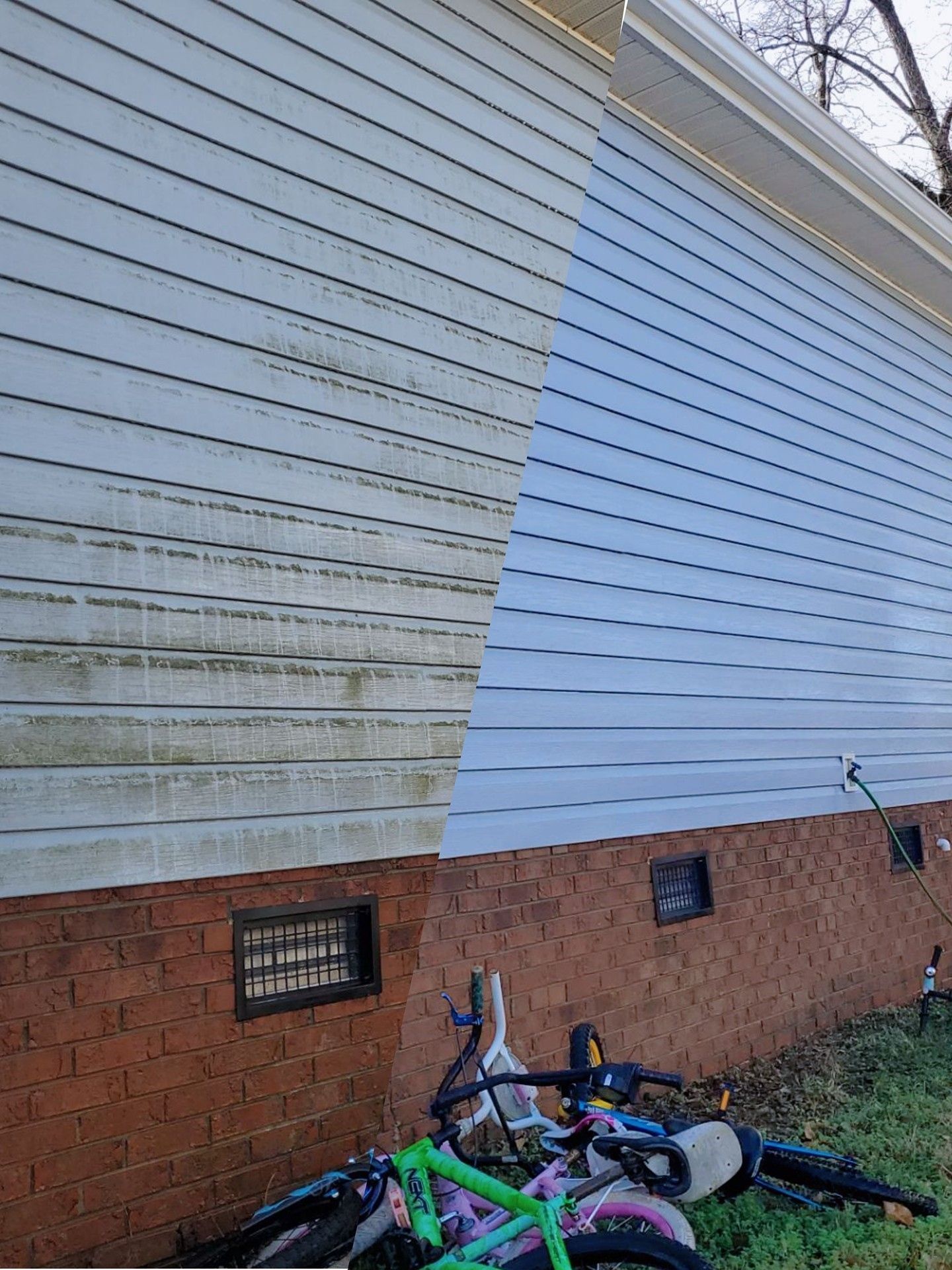 Two bicycles lying on grass against a white clapboard wall and brick foundation.