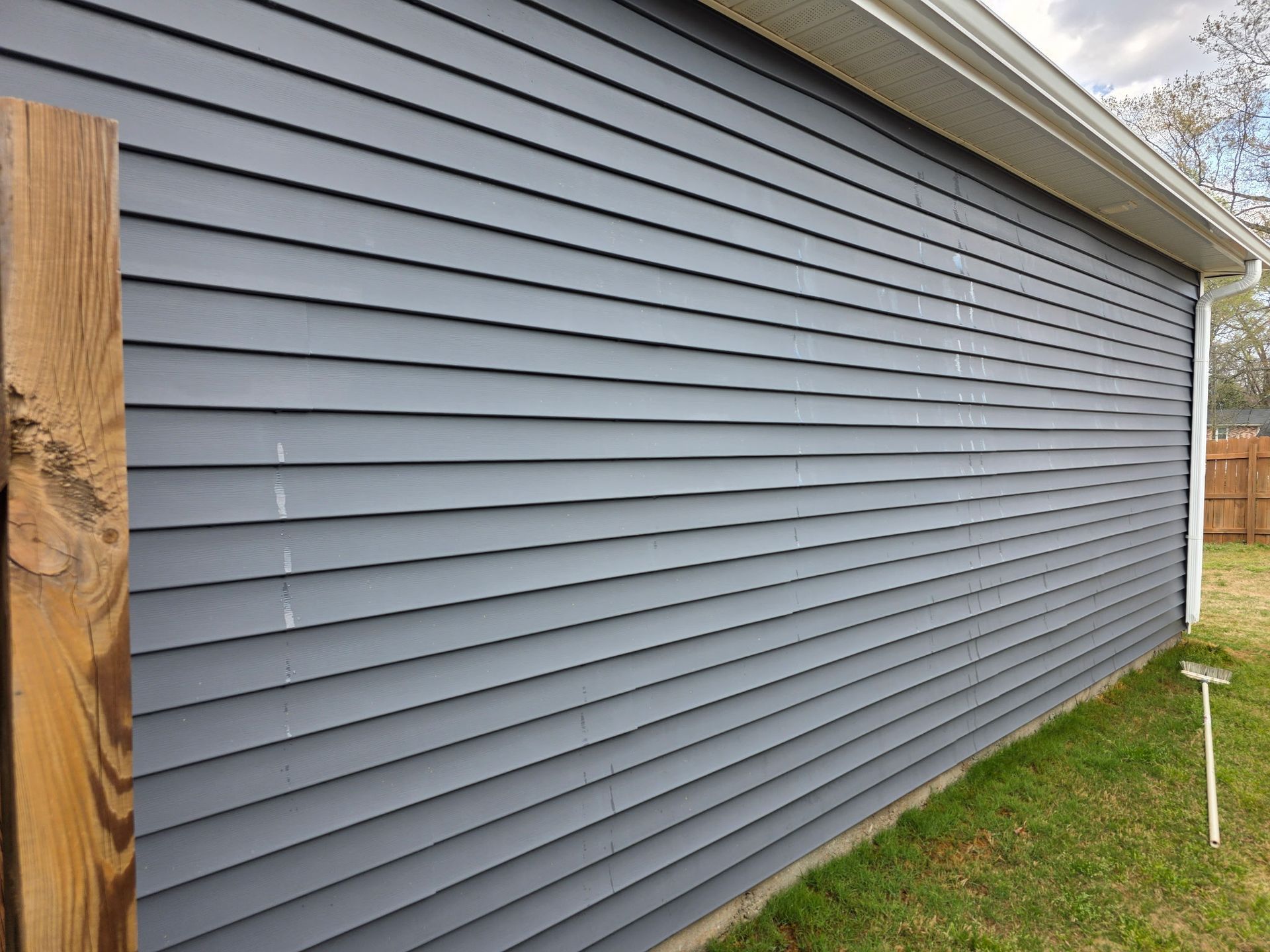 Gray vinyl siding on the side of a house beside a grassy yard and wooden fence post