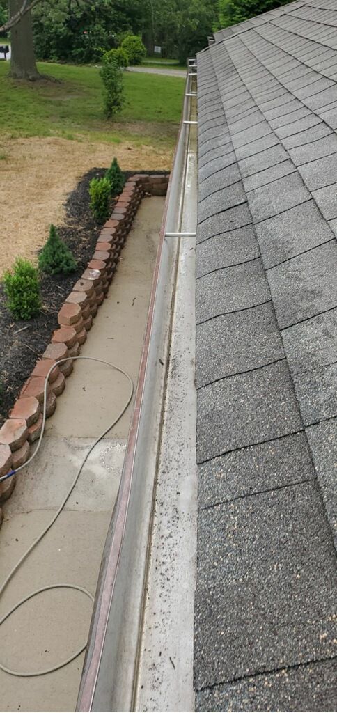 Roof edge with gray shingles, gutter, and a narrow walkway beside a landscaped yard
