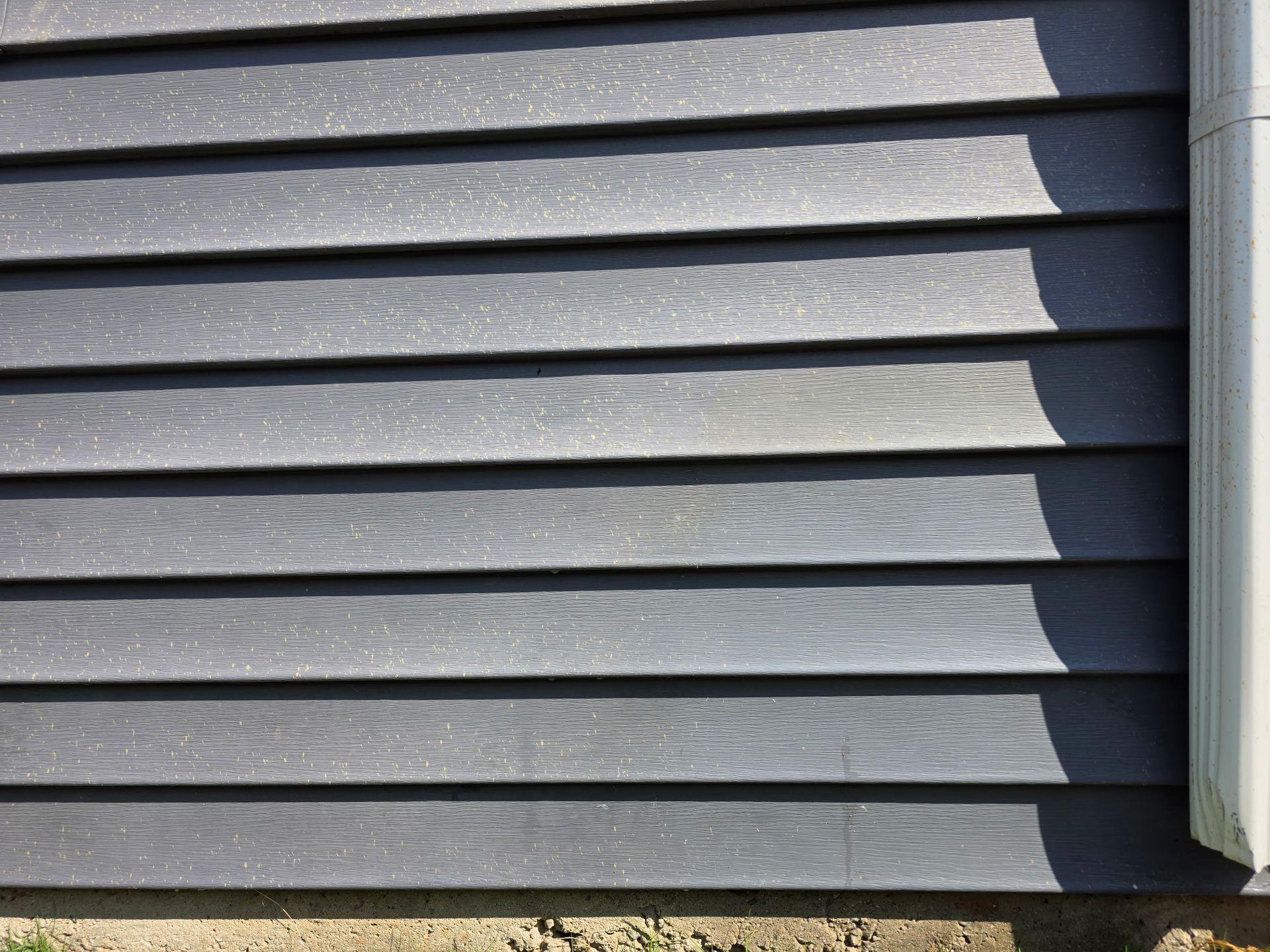 Gray horizontal house siding with a white corner trim in sunlight
