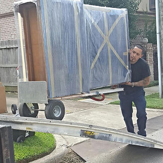 Man moving a large wrapped item on a wheeled dolly down a ramp.