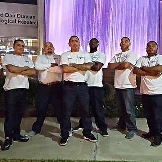 Group of six people standing together, arms crossed, in front of a fountain at night.
