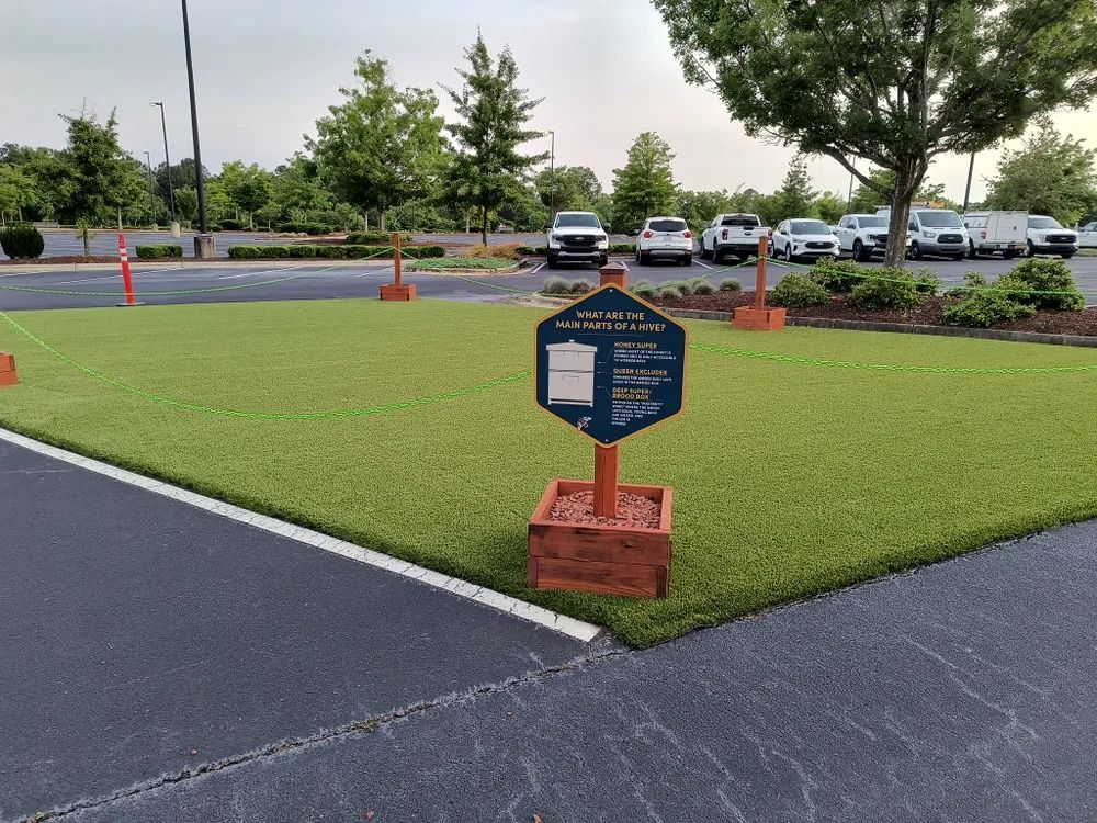 Small landscaped lawn with a blue sign, bordered by pavement and orange cones in a parking lot.