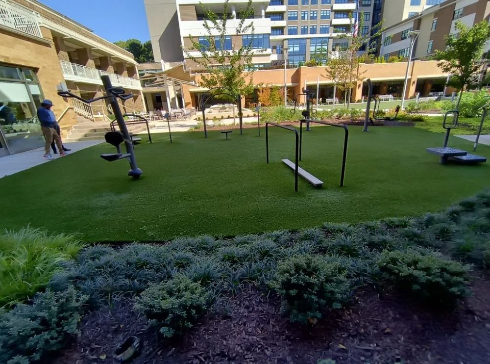 Outdoor courtyard with green turf, exercise equipment, and apartment buildings in the background.