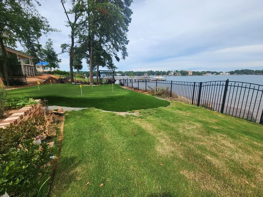 Grassy riverside yard with trees, stone edging, and a black fence along the water