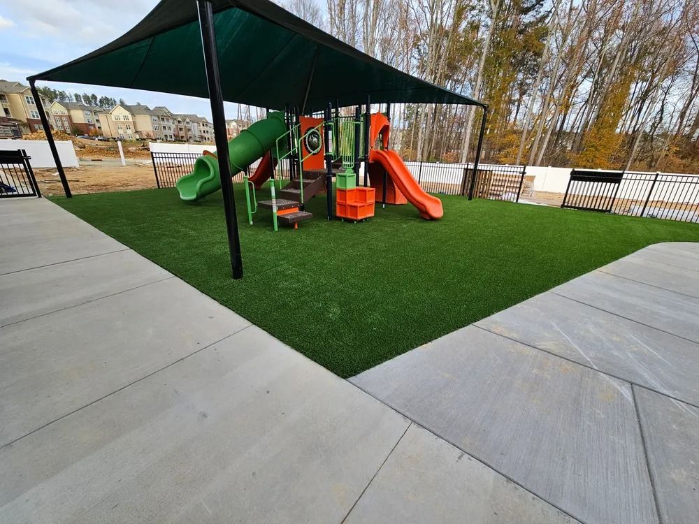 Covered playground with green turf, orange slides, and a green climbing structure