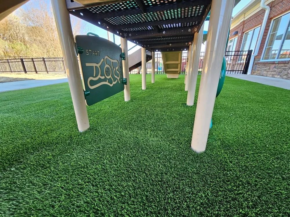 Covered walkway with white posts, green turf, and a brick building beside a fenced lawn.