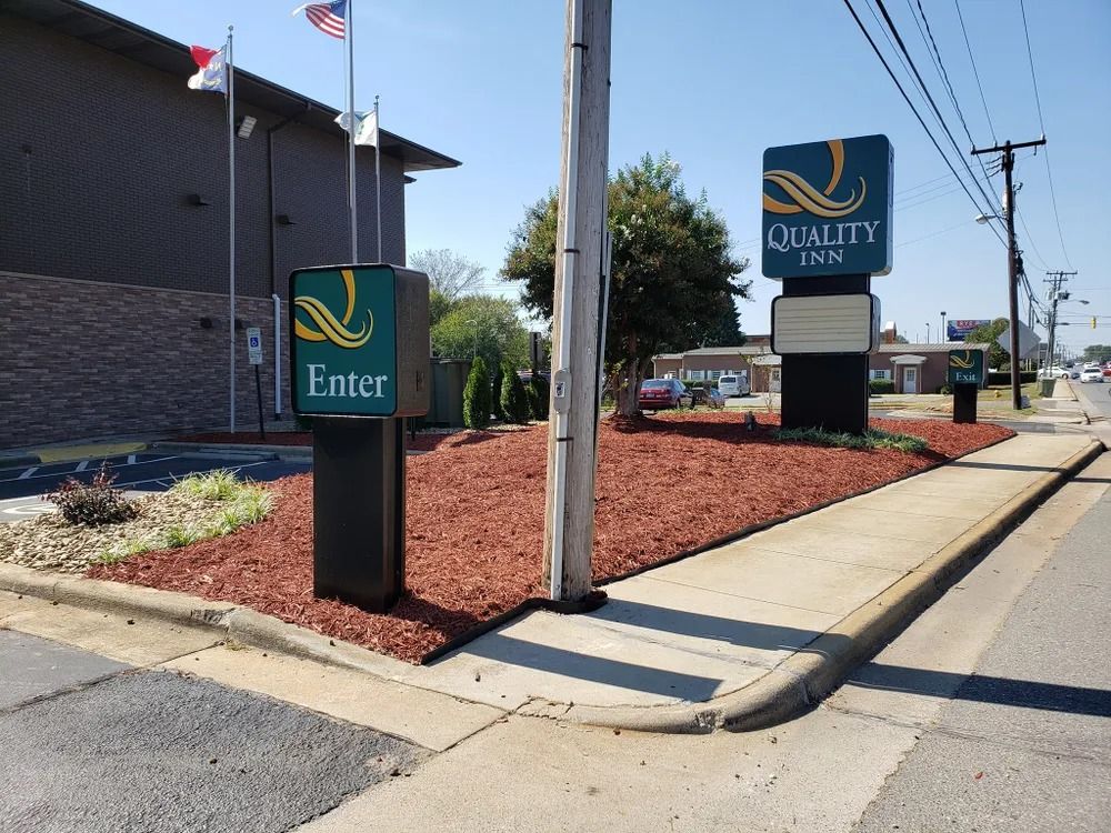 Entrance sign for a brick building with American and Texas flags, beside a sidewalk and road.