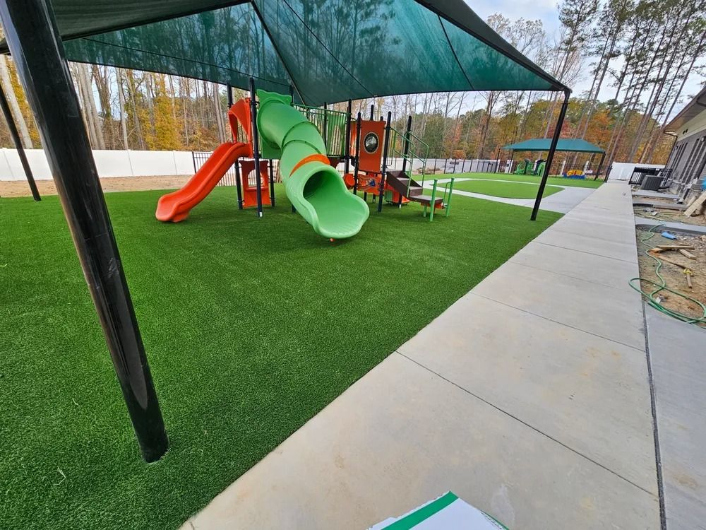 Playground with green and orange slides on artificial turf beside a concrete walkway
