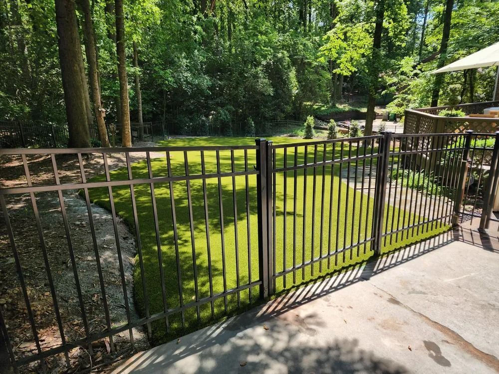 Black metal fence beside a sunny green backyard with trees and a concrete patio