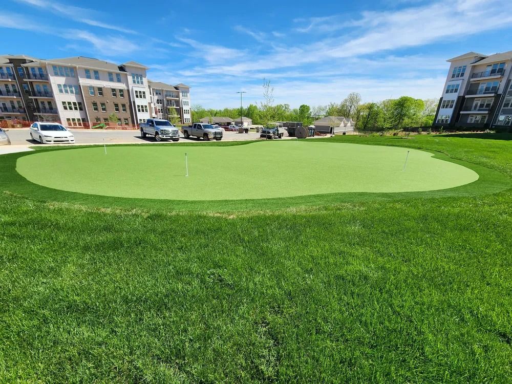 Bright green lawn with a circular putting green in a courtyard between apartment buildings under a blue sky