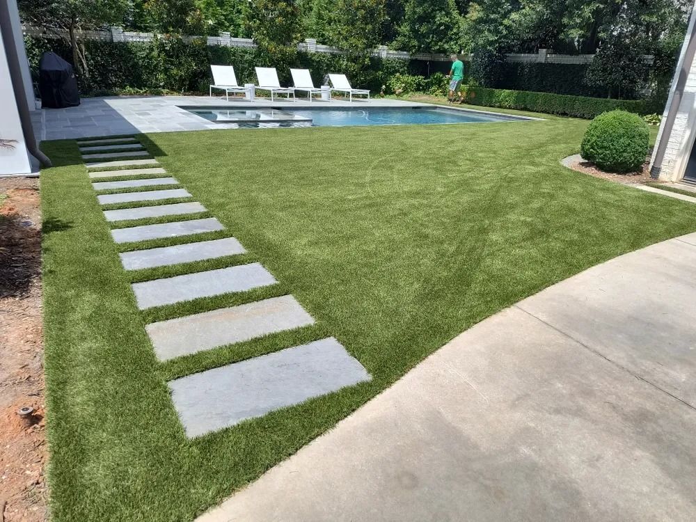 Backyard pool with green lawn, stepping stones, and lounge chairs near a hedge-lined patio