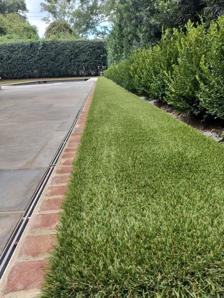 Driveway beside a neatly trimmed green hedge and lawn with a brick border