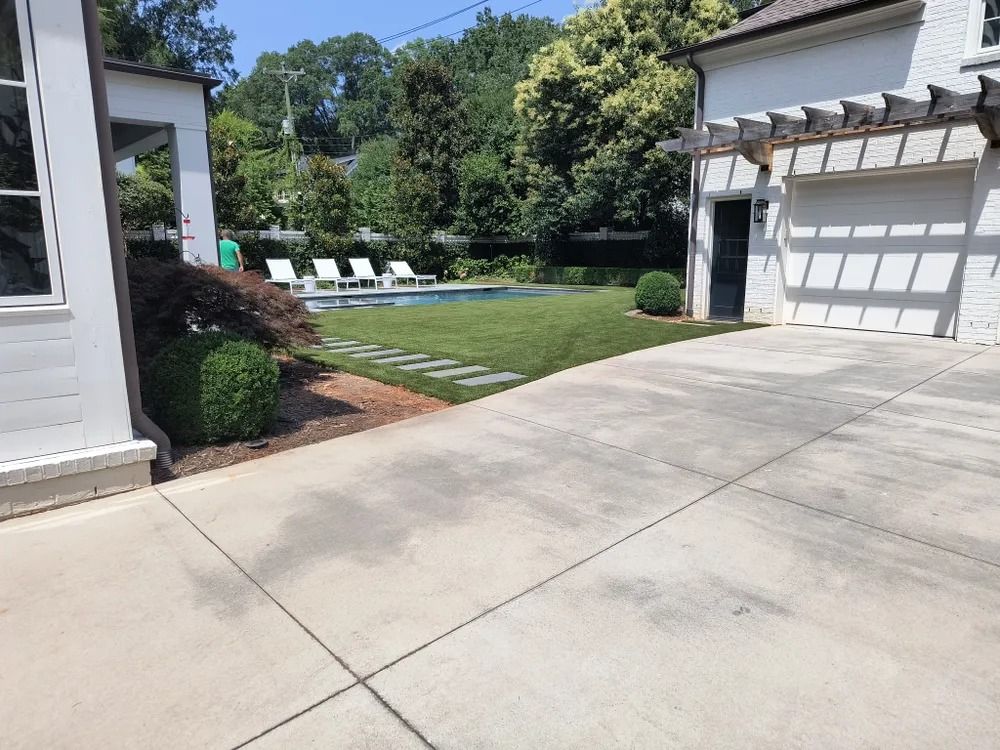 Driveway beside a white house leading to a backyard with a swimming pool and lounge chairs