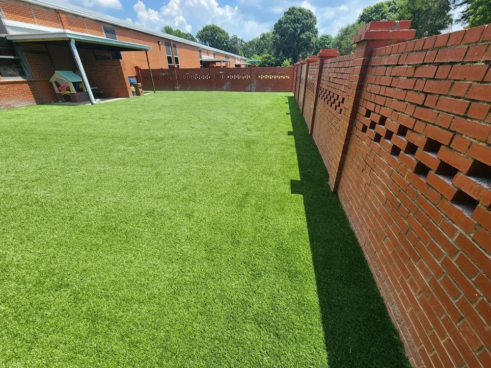 Bright green lawn beside a brick wall and brick buildings under a sunny sky