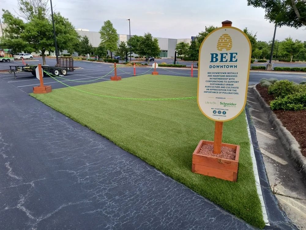 Bee Habitat sign on a lawn beside a parking lot with orange cones and a blacktop path
