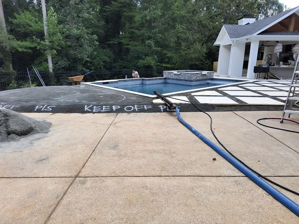 Pool deck under construction with hoses and a “KEEP OFF” warning painted on the surface.