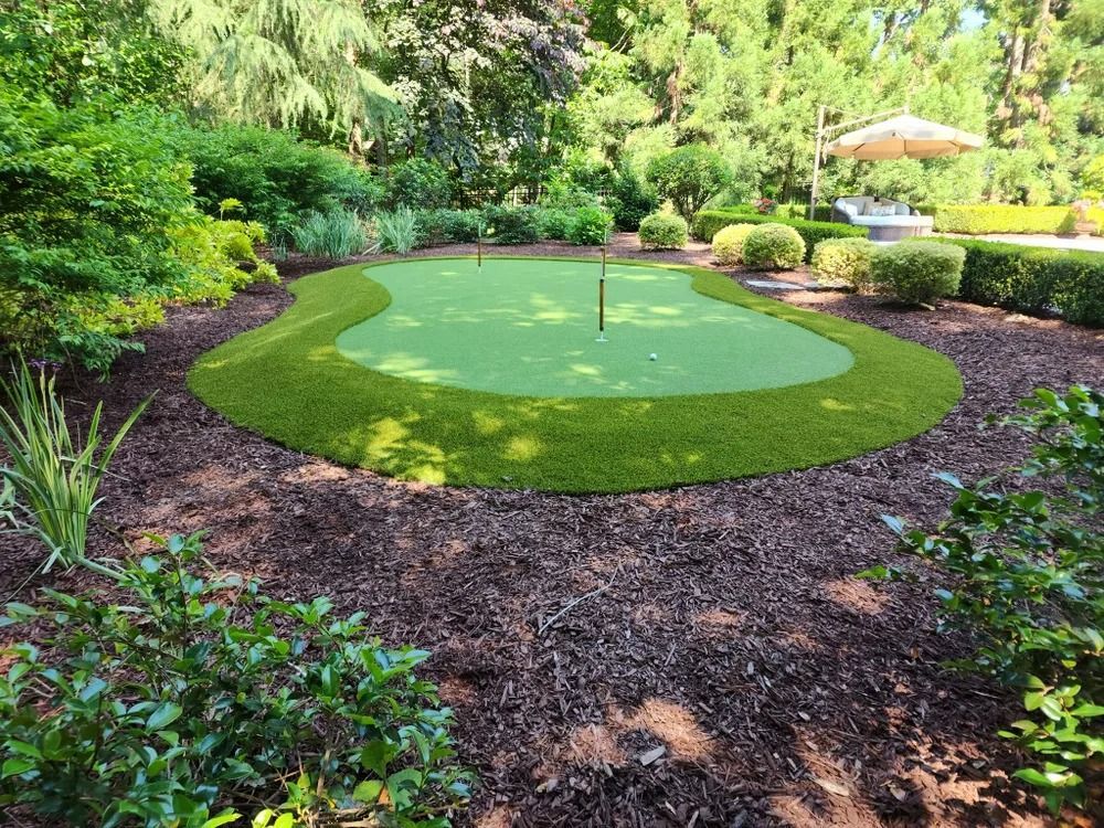 Lush garden with a small circular putting green and flagstick, surrounded by trees and shrubs.