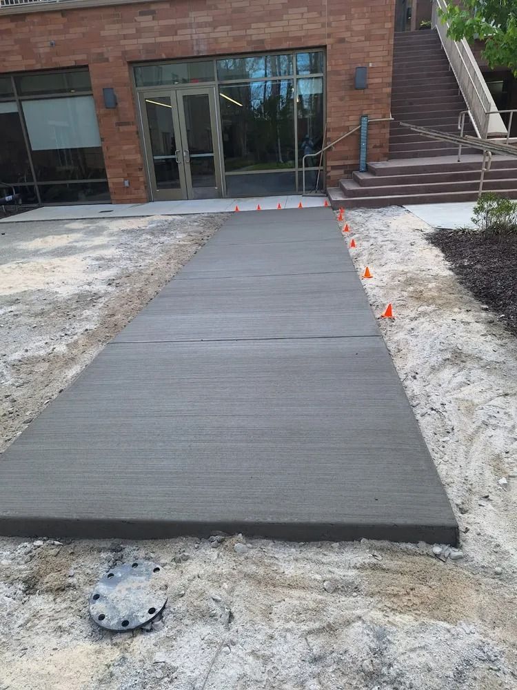 New concrete sidewalk ramp leading to a brick building entrance, with orange markers along the right edge.