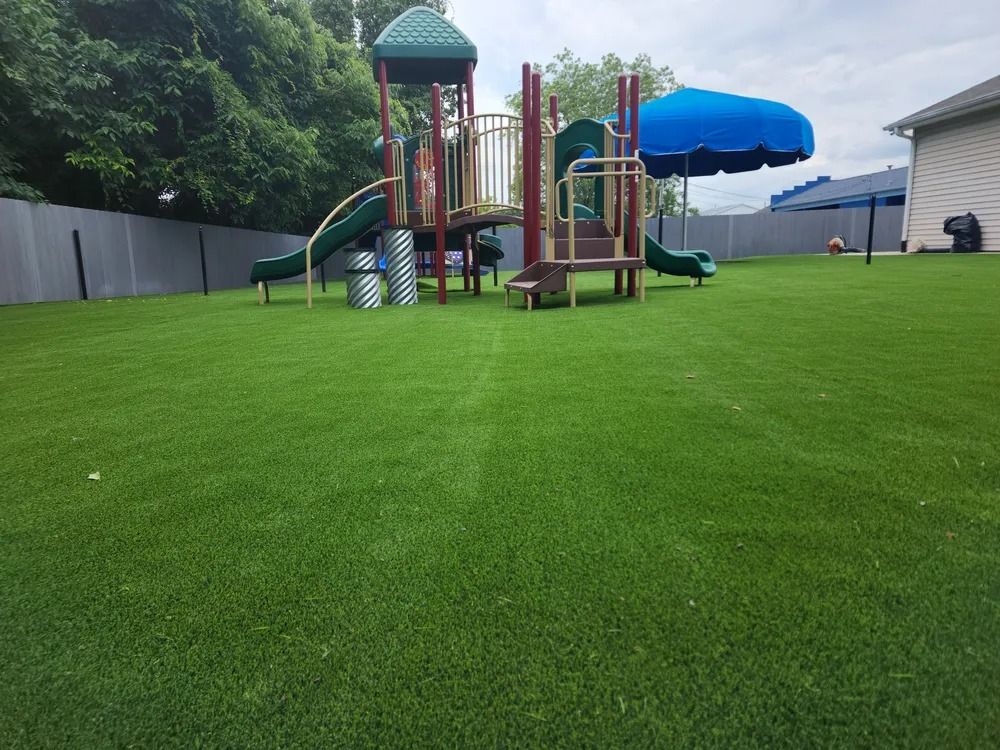 Playground on bright green turf with slides, climbing structures, and a blue umbrella under a cloudy sky