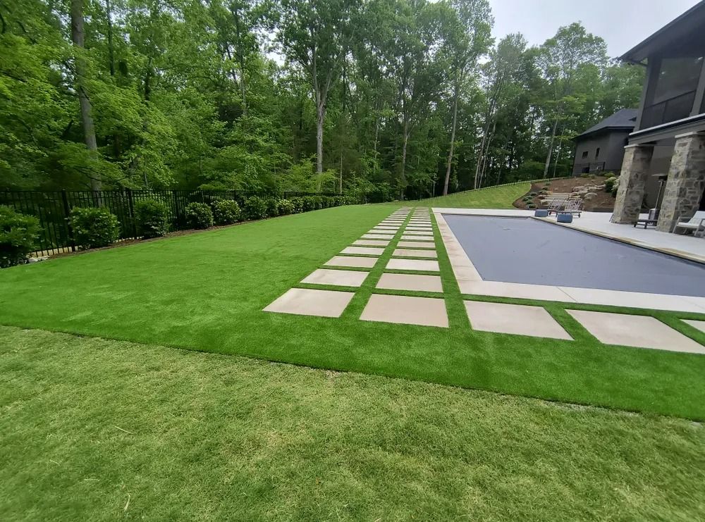 Landscaped backyard with stone paver path, green lawn, trees, and a patio beside a house