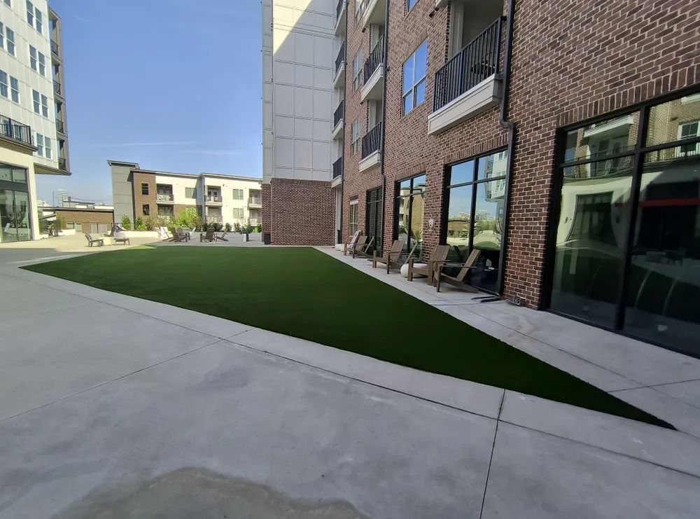 Modern apartment courtyard with brick building, concrete walkway, and green artificial lawn
