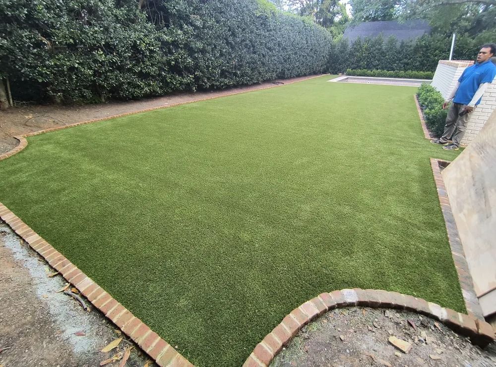 Freshly laid green turf in a landscaped backyard beside a stone patio and tall hedge
