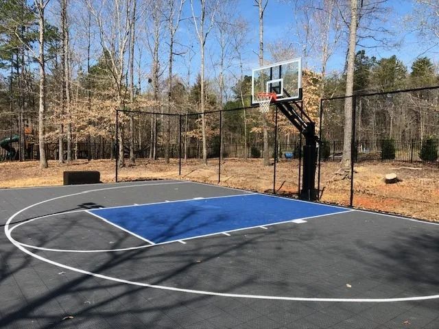 Outdoor basketball court with a blue painted key and hoop, surrounded by trees and a chain-link fence