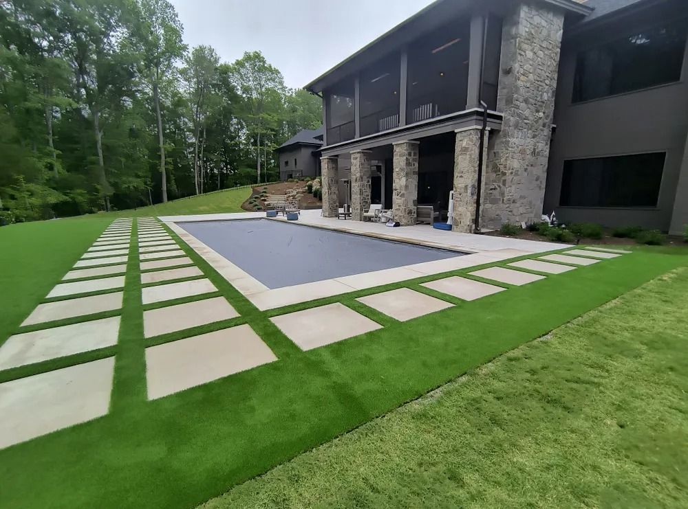 Modern house with stone columns, a patio, and a geometric concrete walkway beside a green lawn.