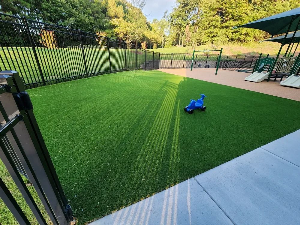 Backyard with black fence, artificial turf, and a small blue toy car near patio chairs