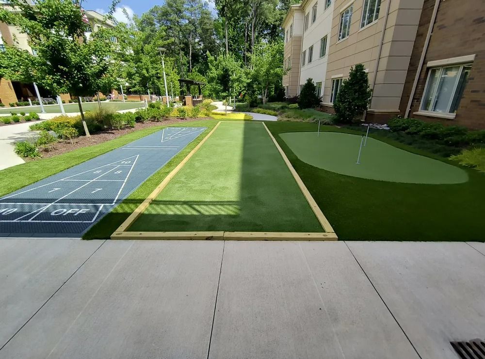 Outdoor fitness area with blue shuffleboard-style court and green turf lanes beside an apartment building