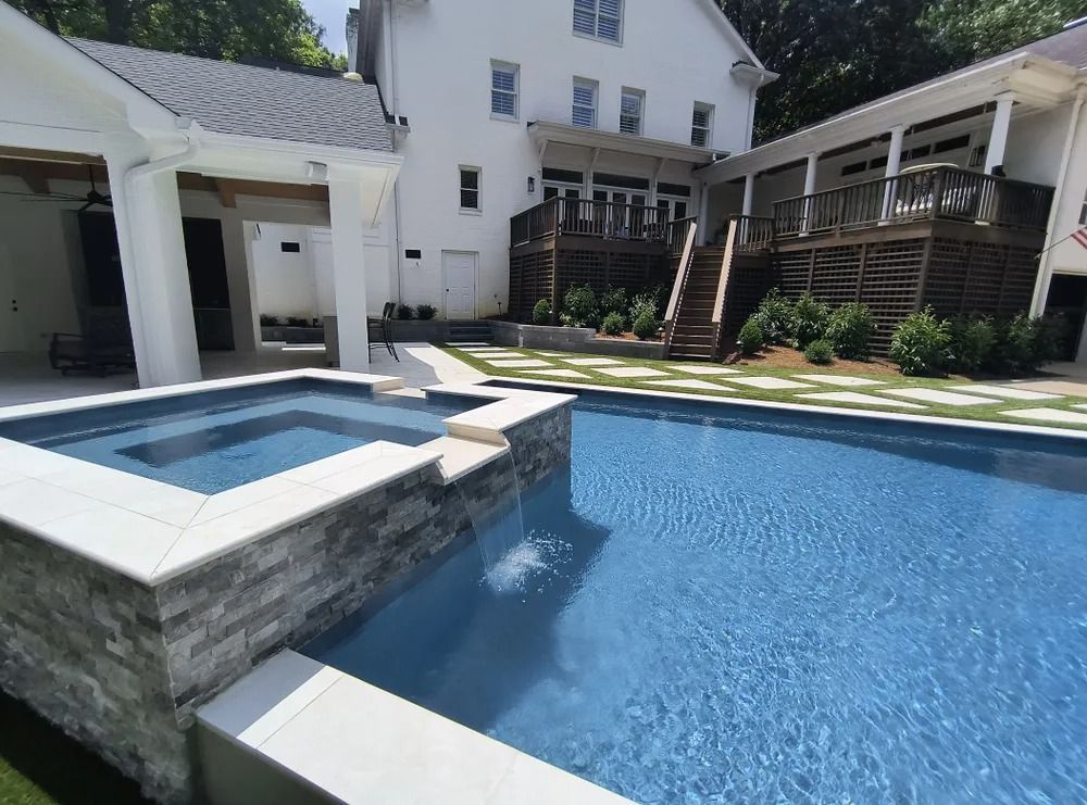 Blue backyard pool with attached hot tub beside a white house and shaded patio pergola