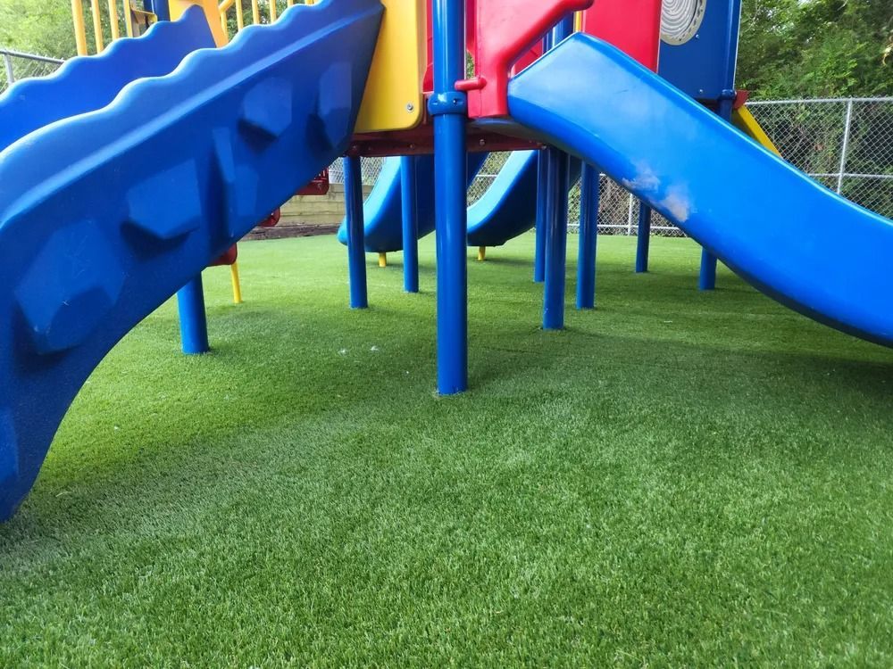 Blue playground slide over green artificial turf with support poles beneath