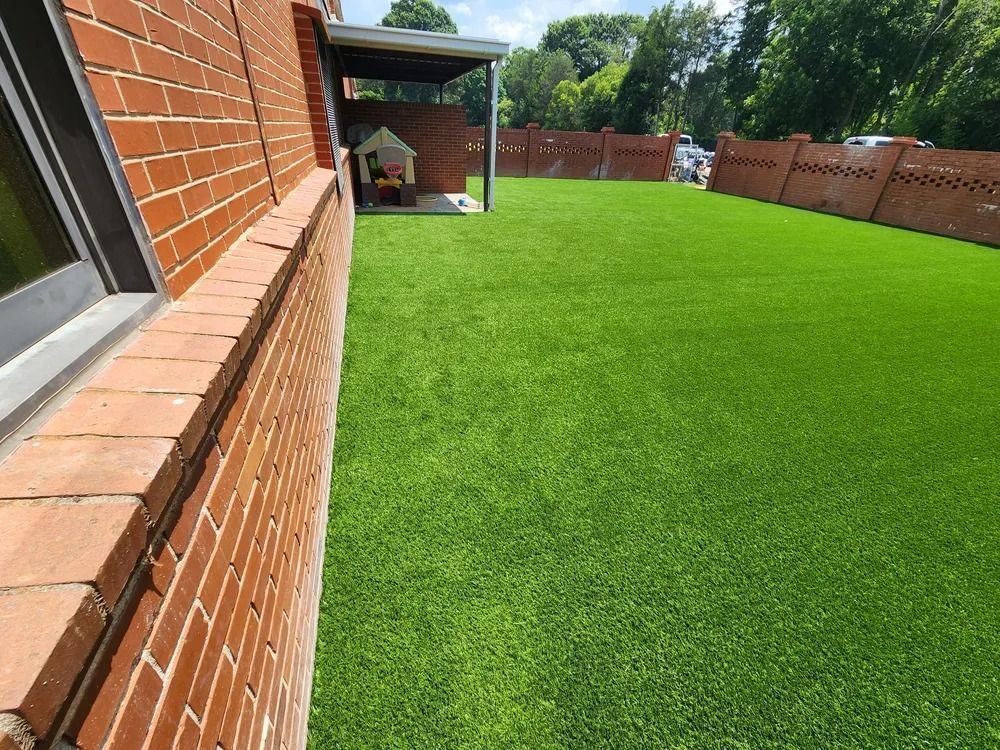 Brick house wall beside a bright green lawn and covered patio in a fenced backyard